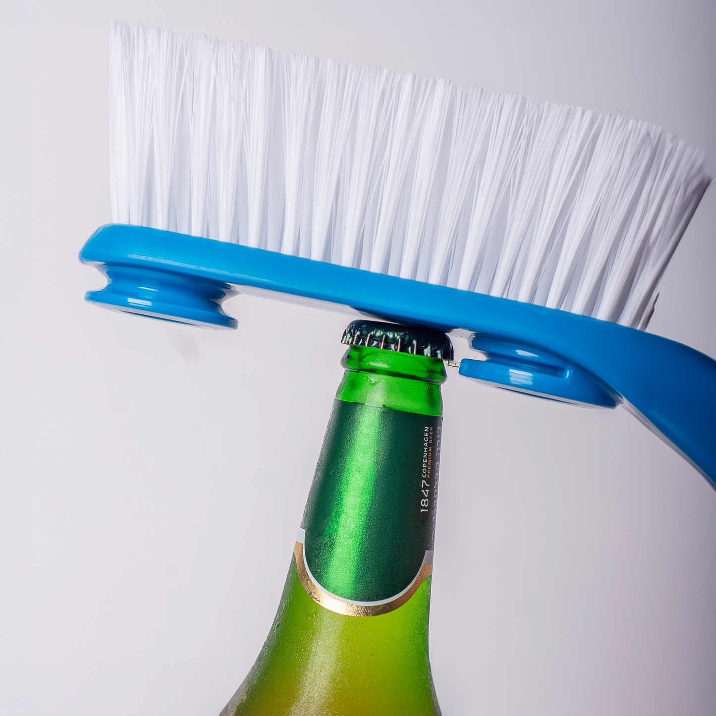 Blue cleaning brush with white bristles gripping the cap of a green glass bottle