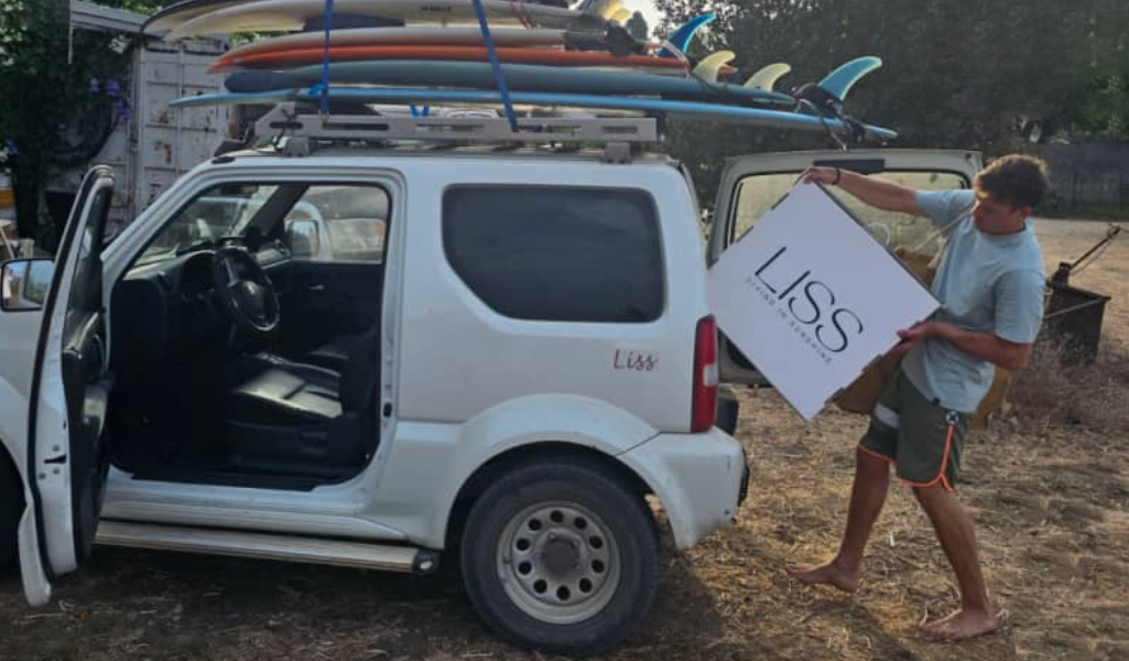 Man loading a LISS branded box into a white car with surfboards on the roof
