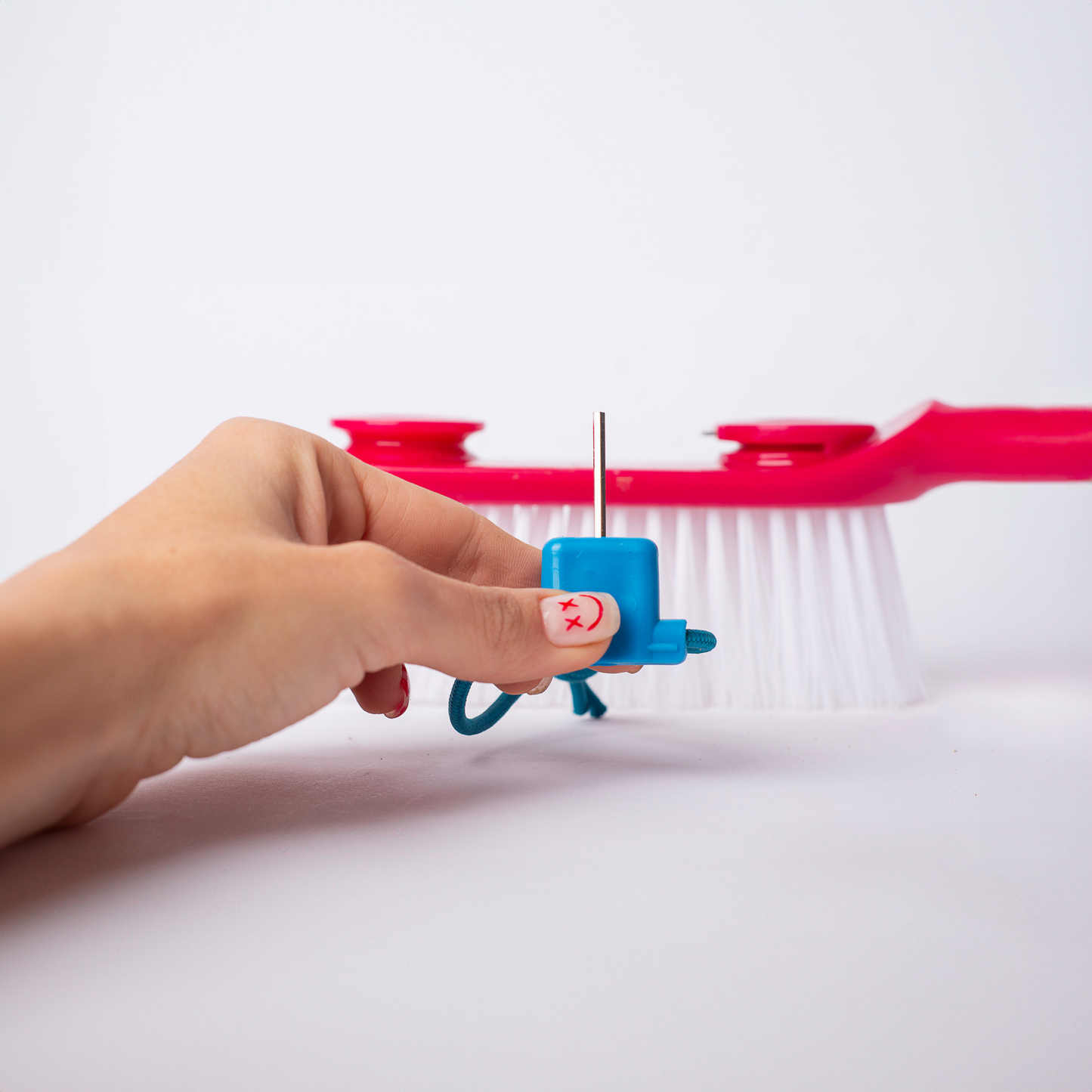 Hand holding small blue tool in front of red and white cleaning brush on white surfac
