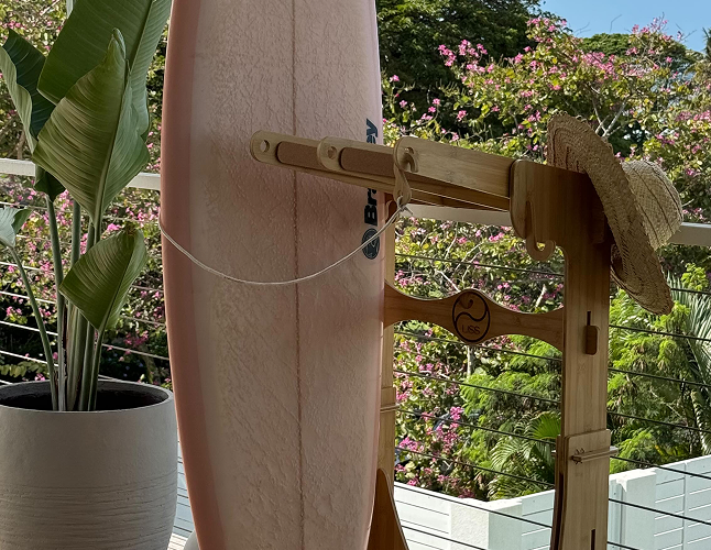 Surfboard on wooden stand with straw hat, balcony view and plants