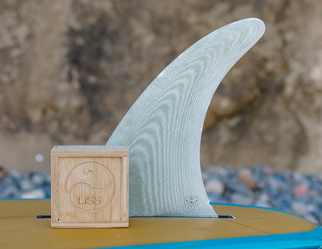 Surfboard fin on a blue board with wooden box engraved with LBS logo on the beach