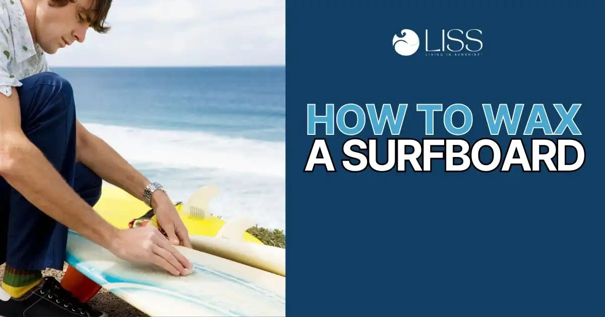 Man waxing a surfboard by the beach with a clear sky and waves in the background.