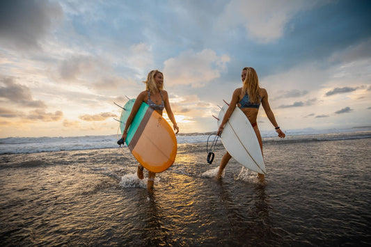 Two people walking holding surfboards