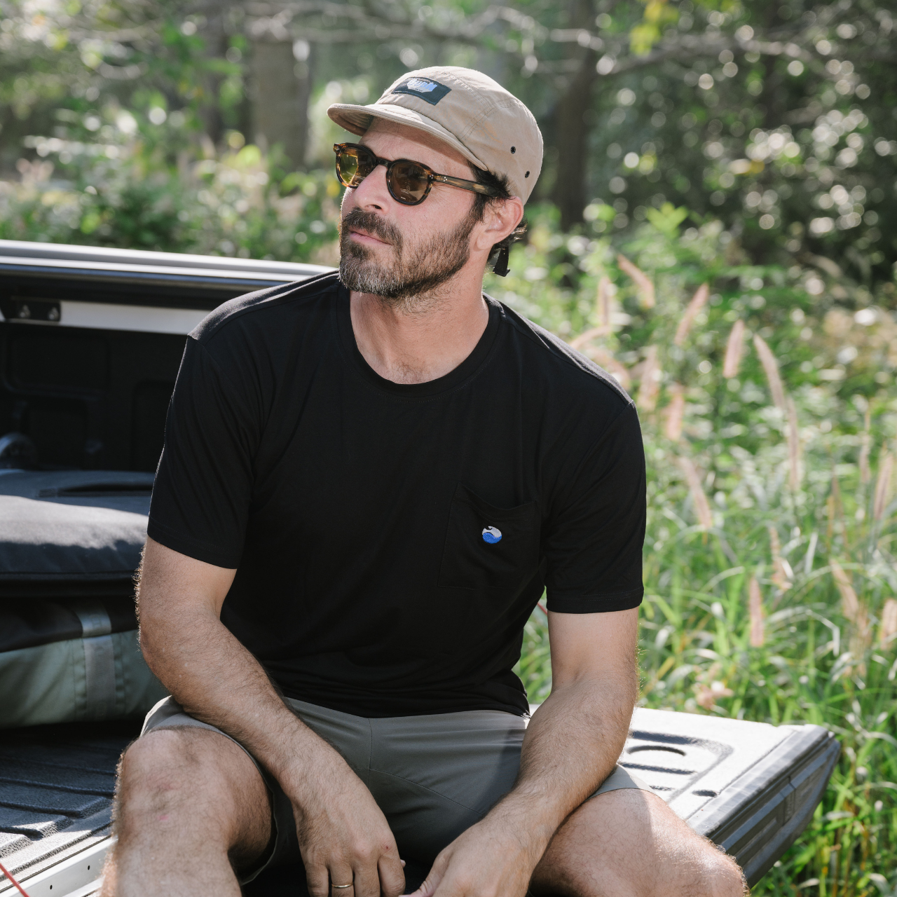 Man in black shirt and cap wearing sunglasses sitting on truck bed outdoors