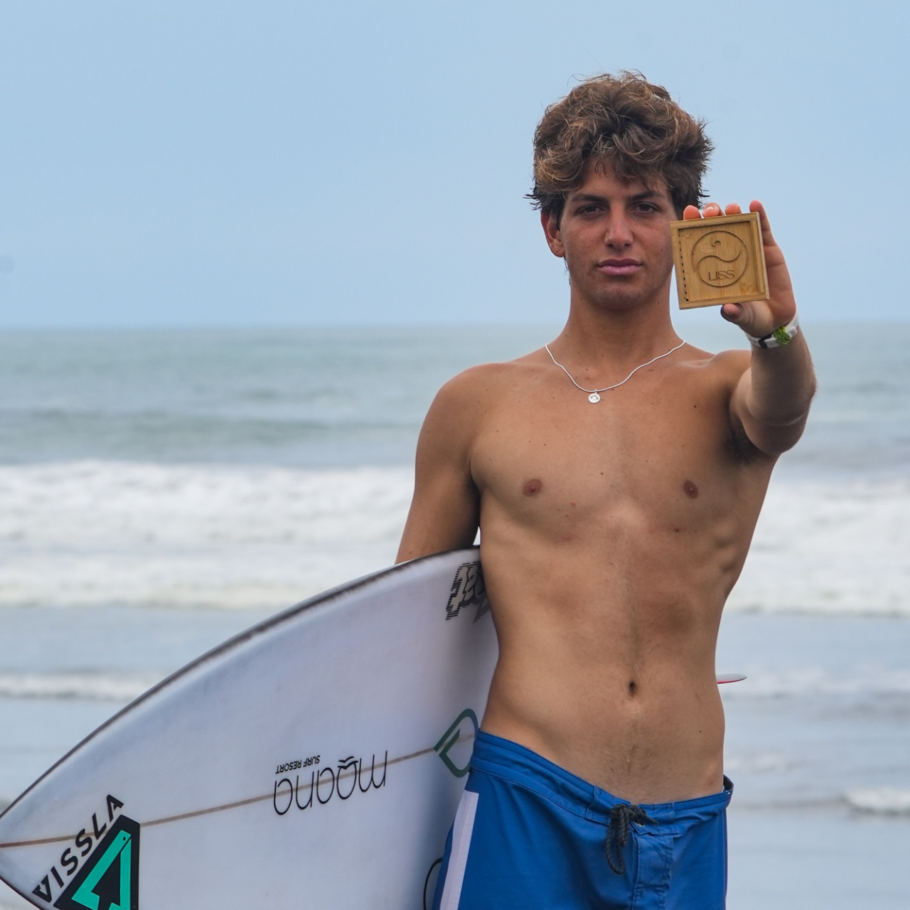 Surfer holding LISS bamboo box while standing with surfboard at the beach