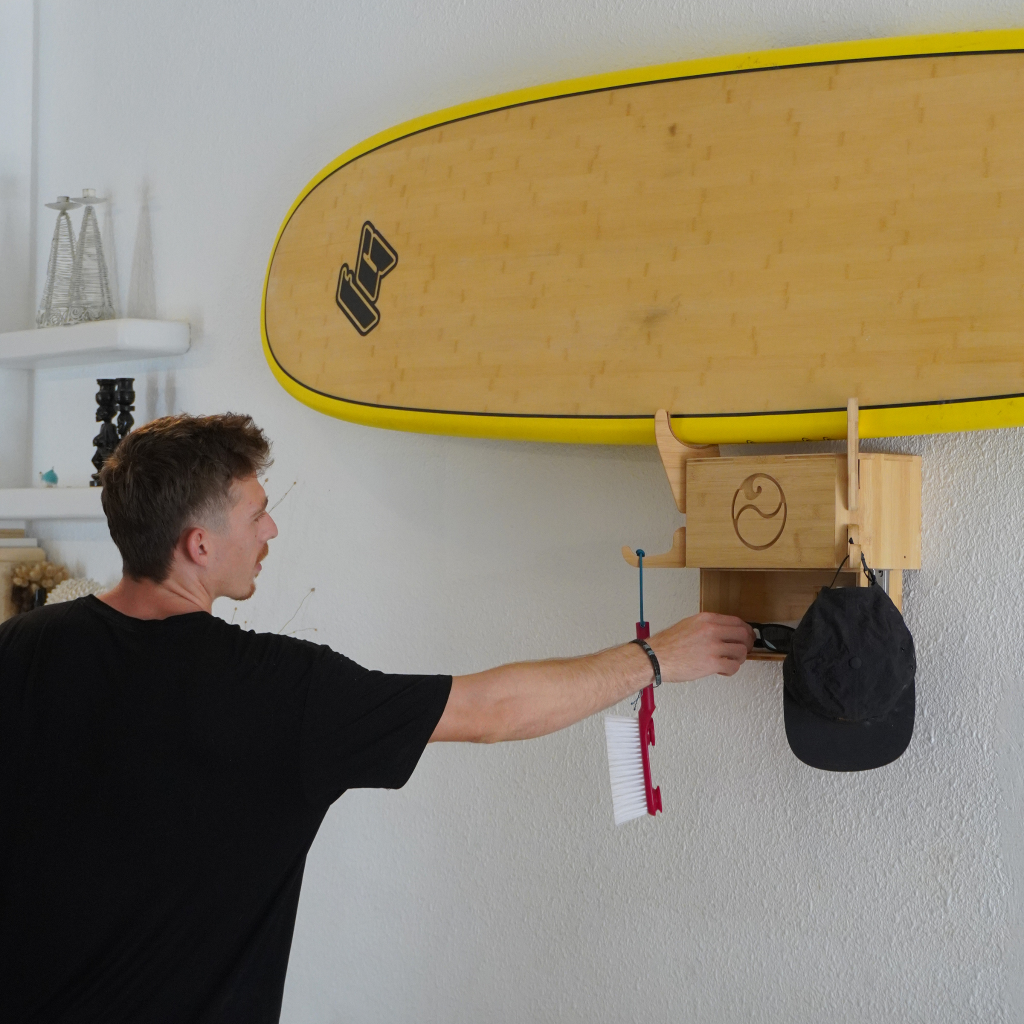 Man using a bamboo wall-mounted surfboard rack with hooks and storage drawer.